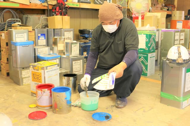 倉庫で色見本を見ながら塗料を調合する職人