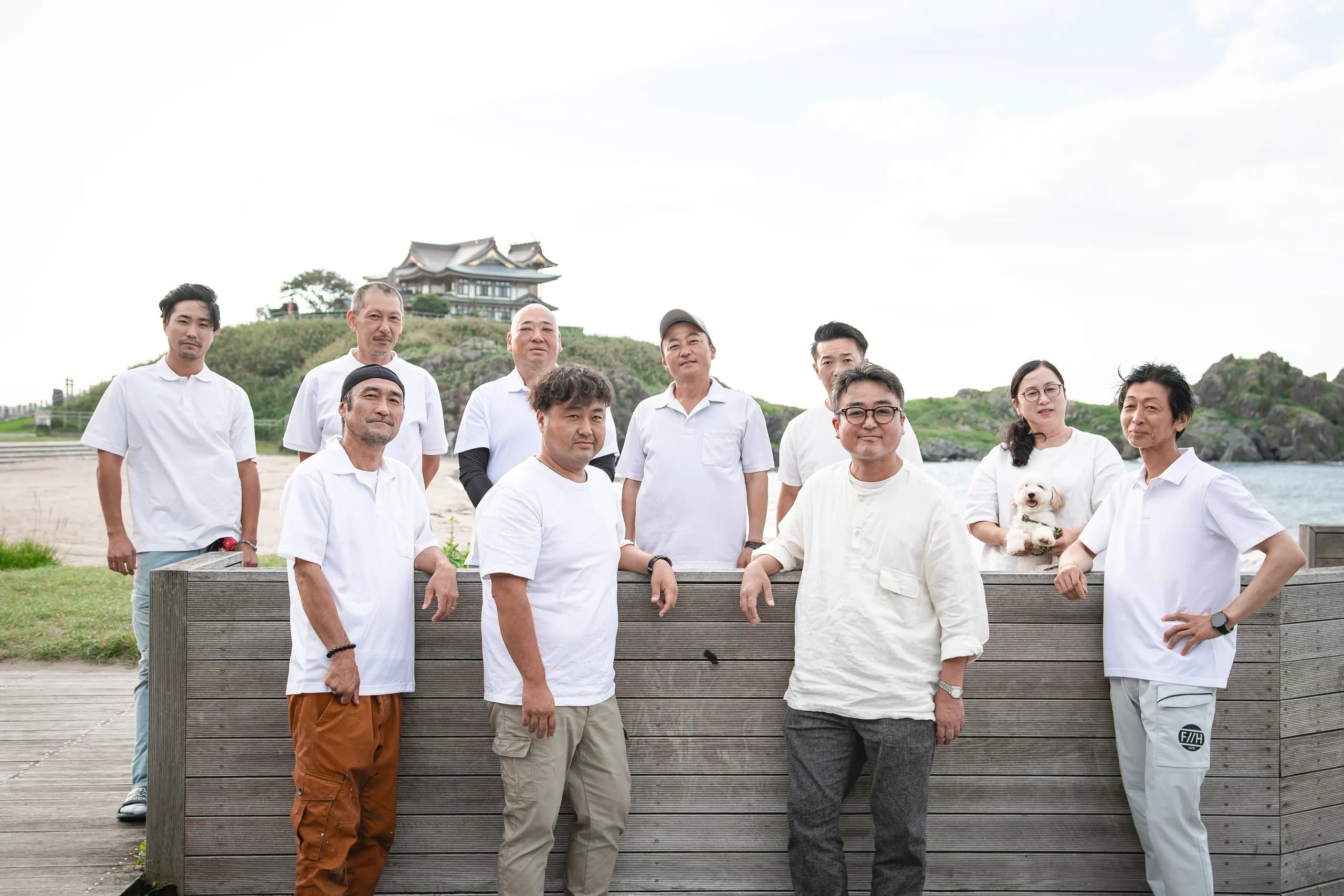 海辺のウッドデッキに並ぶ、八戸ペイントの社員たちの集合写真