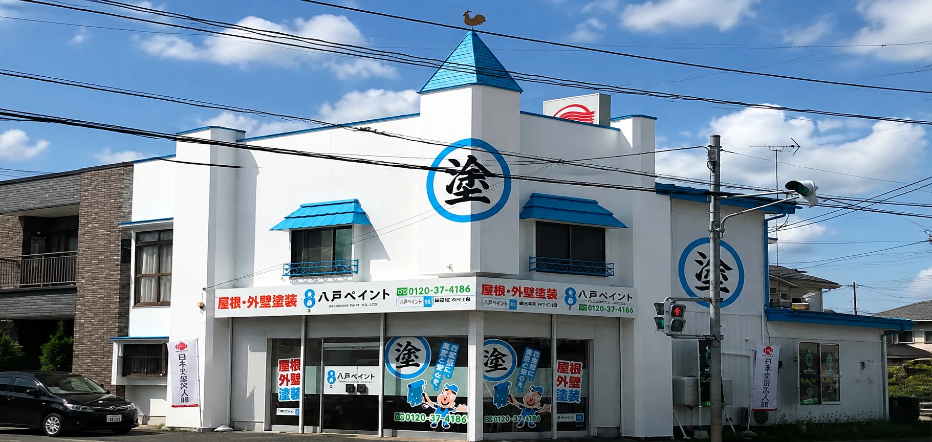 斜めから見た八戸ペイントの社屋。青い尖り屋根の塔屋と、丸に「塗」の看板