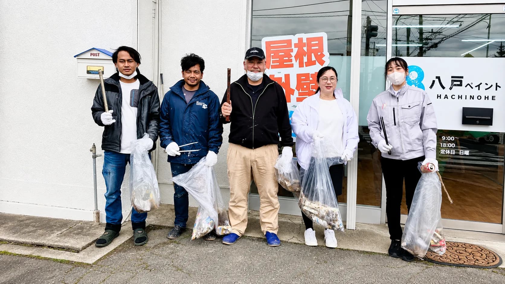 会社の前で、ごみ袋とトングを持って並ぶ八戸ペイントの社員5人