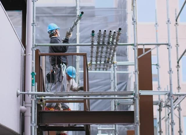 足場の上で単管を受け渡す作業員
