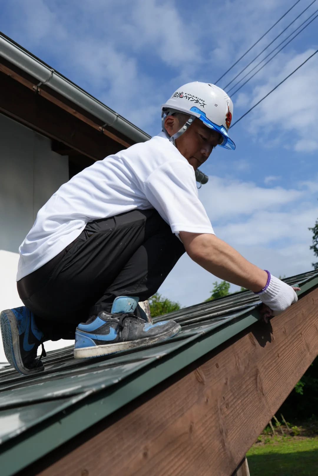 屋根の上にかがみ込み、軒先の際に手を入れる八戸ペイントの職人